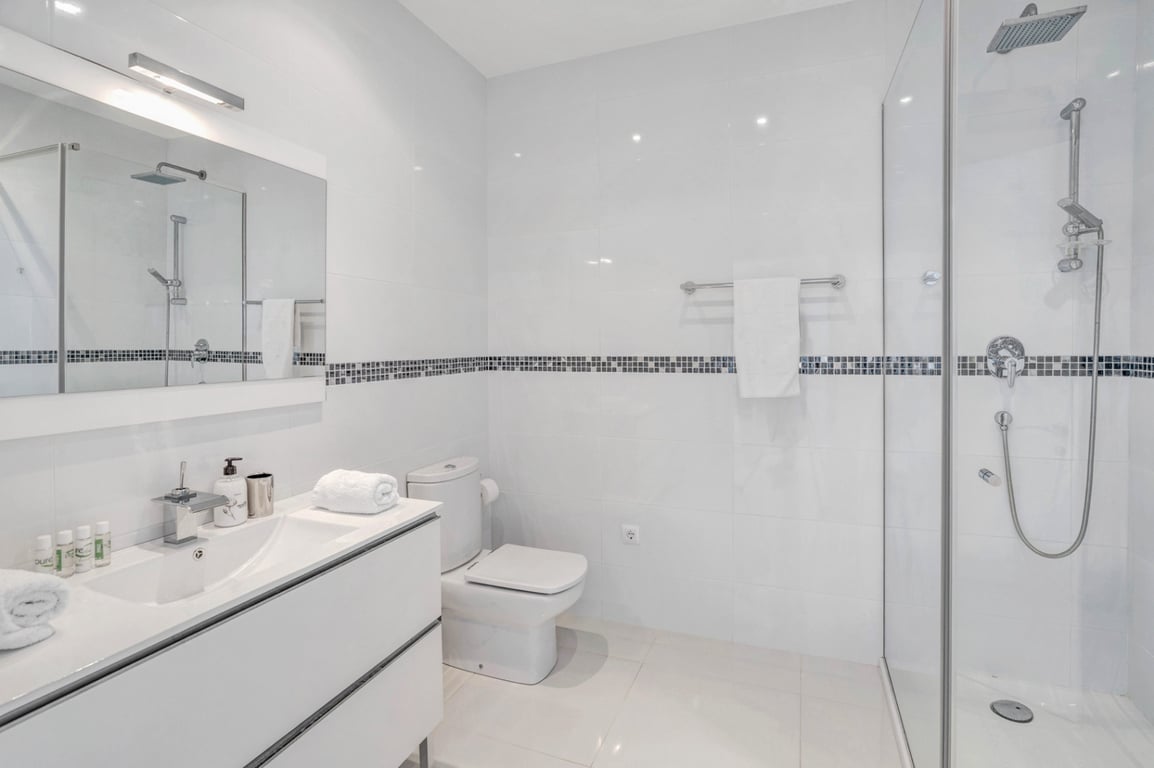 Moderne badkamer met witte tegels en mozaïekrand, een strak wit badmeubel en een inloopdouche met glazen wand en chromen regendouche.