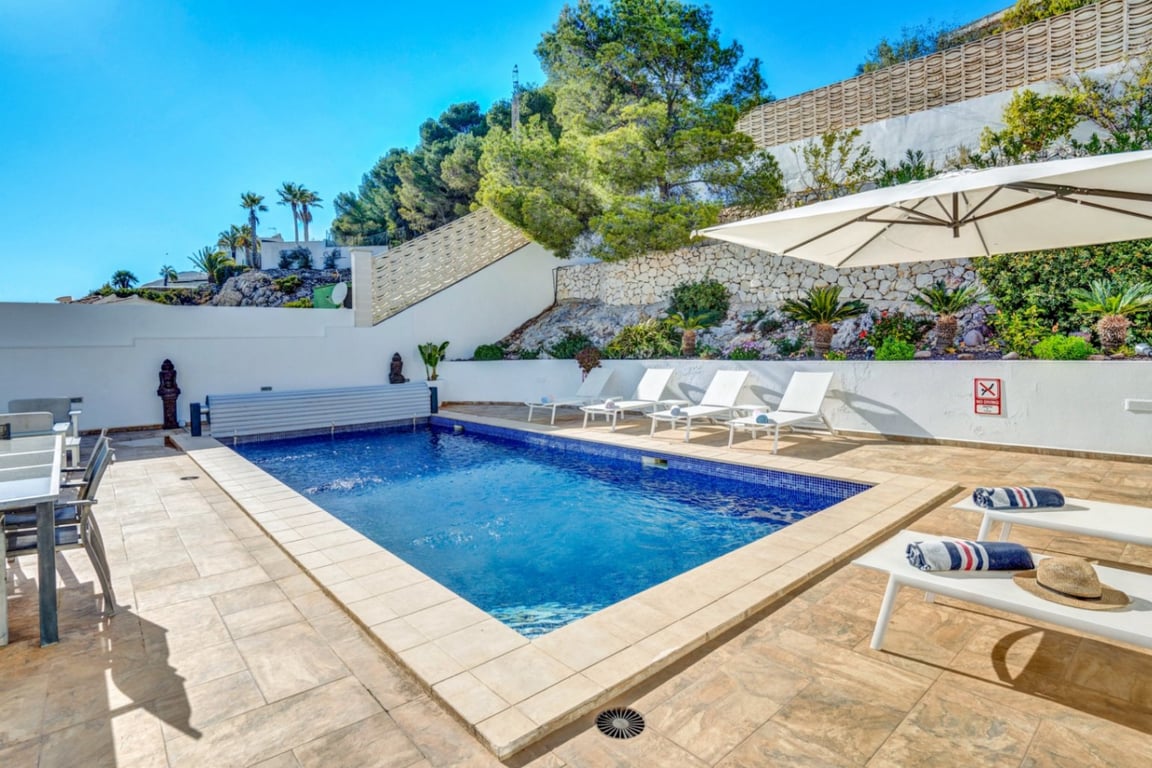 Privé-buitenzwembad met blauw mozaïek, ruim zonneterras met witte ligbedden en een natuurstenen muur passend bij de mediterrane tuin.