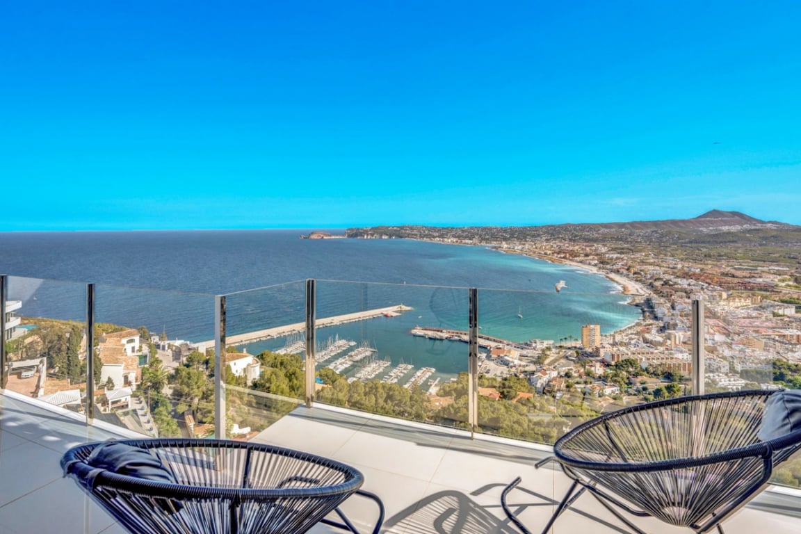 Terras met glazen balustrade en zwarte Acapulco-stoelen, met een panoramisch uitzicht over de haven van Jávea en de Middellandse Zeekust.