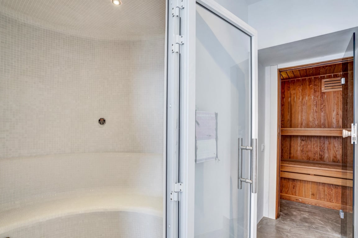 Wellnessruimte met een Turks stoombad in wit mozaïek en een aangrenzende Finse sauna met houten afwerking voor optimaal comfort.