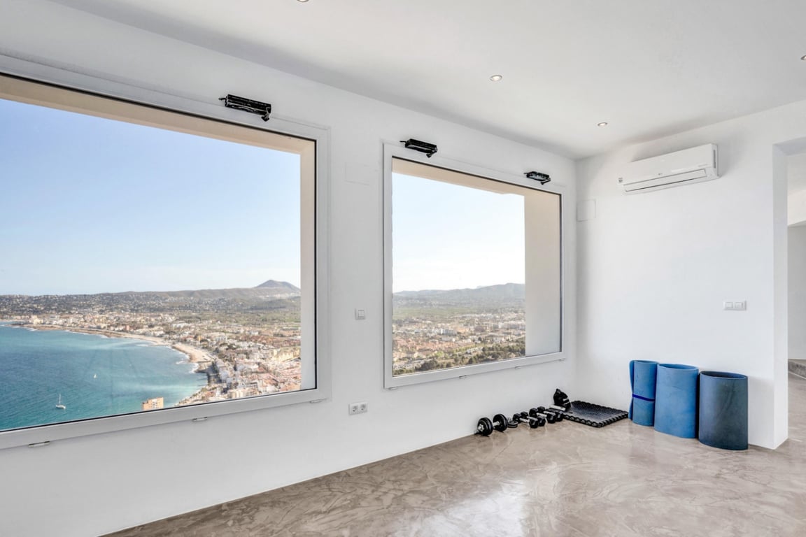 Yoga- en fitnessruimte met een gepolijste microcementvloer en grote ramen met panoramisch uitzicht over de baai van Jávea en de zee.