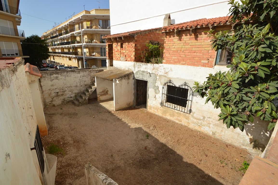 Besloten patio met onverharde grond, bakstenen bijgebouwen en een buitentrap, gelegen in een authentieke stedelijke omgeving met veel potentieel.