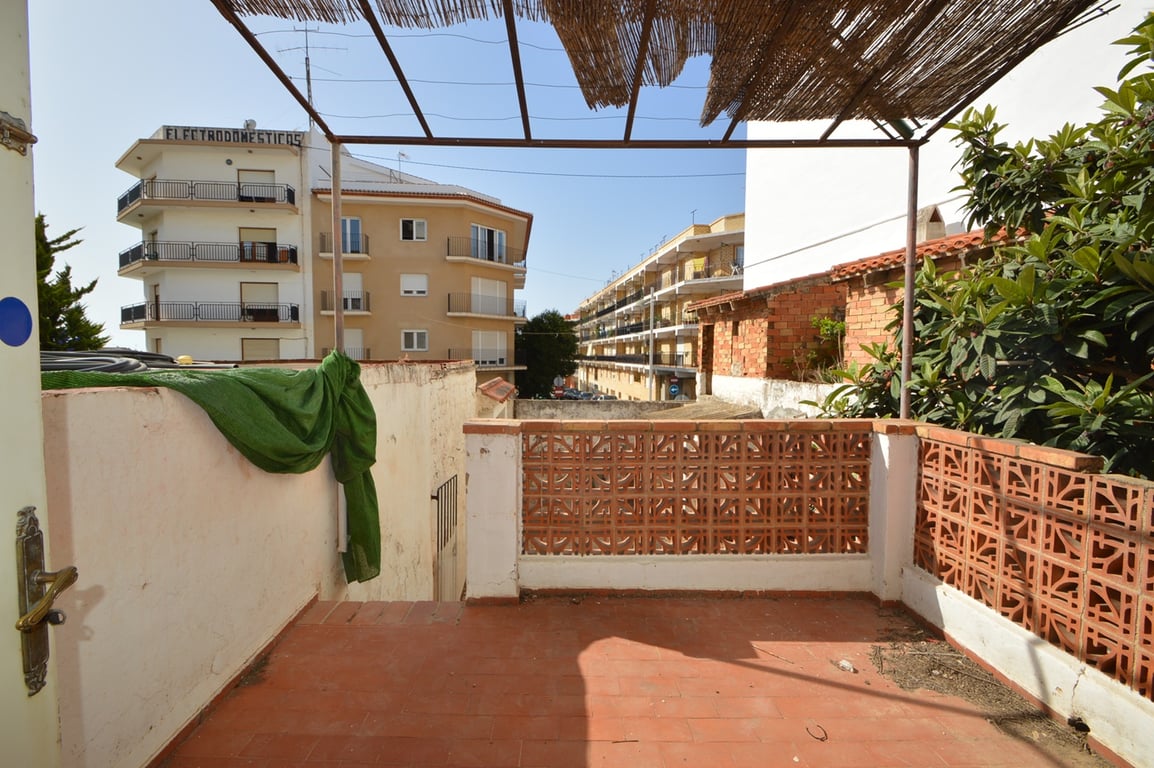 Buitenterras met terracotta tegels en decoratief metselwerk, overdekt door een metalen pergola met rieten matten en uitzicht op de stedelijke omgeving.