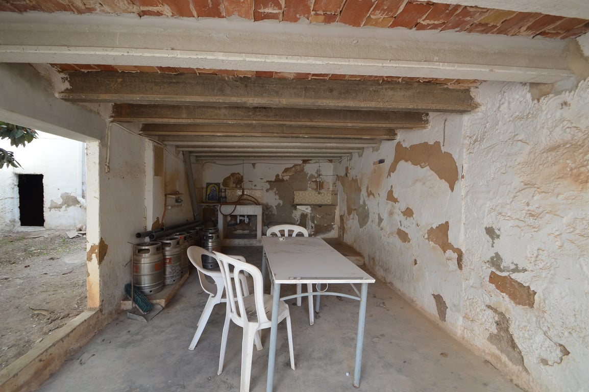 Overdekt terras met een plafond van betonbalken en baksteen, een authentieke ruimte met potentieel voor een buitenkeuken of hobbyruimte.