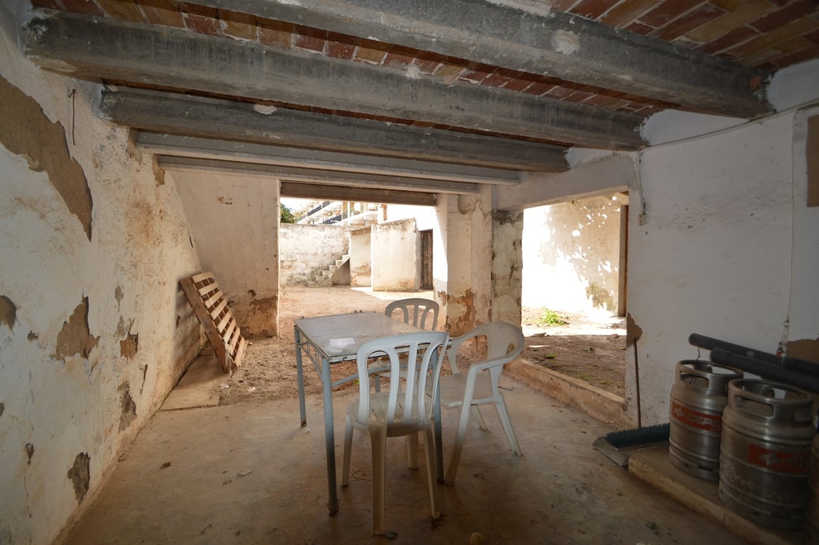 Overdekte veranda met betonnen balken en bakstenen gewelven, die direct toegang biedt tot de besloten binnentuin en patio.