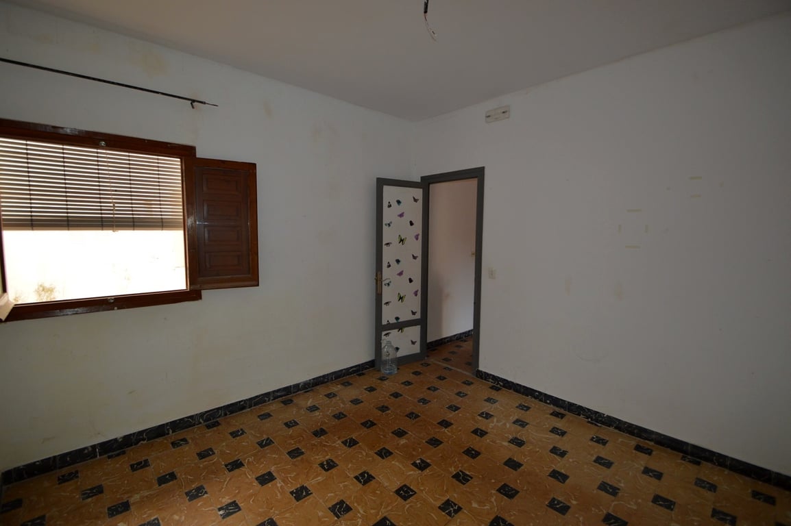 Slaapkamer met traditionele patroontegels, witte muren en een houten raam met luiken. Een te renoveren ruimte met veel mogelijkheden.