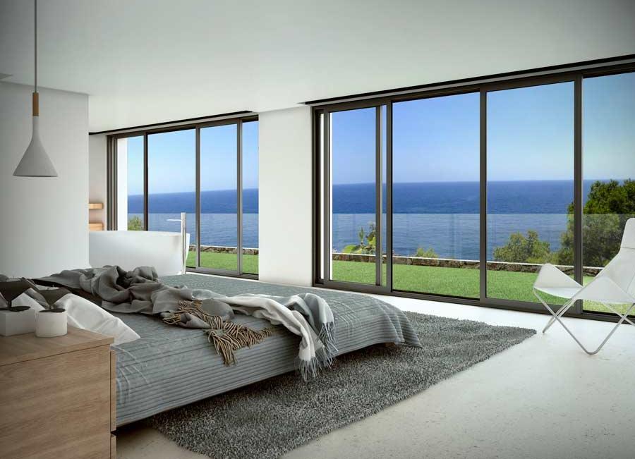 Minimalistische slaapkamer met kamerhoge glazen schuifdeuren, grijze textielaccenten en panoramisch uitzicht op de Middellandse Zee over een verzorgd gazon.