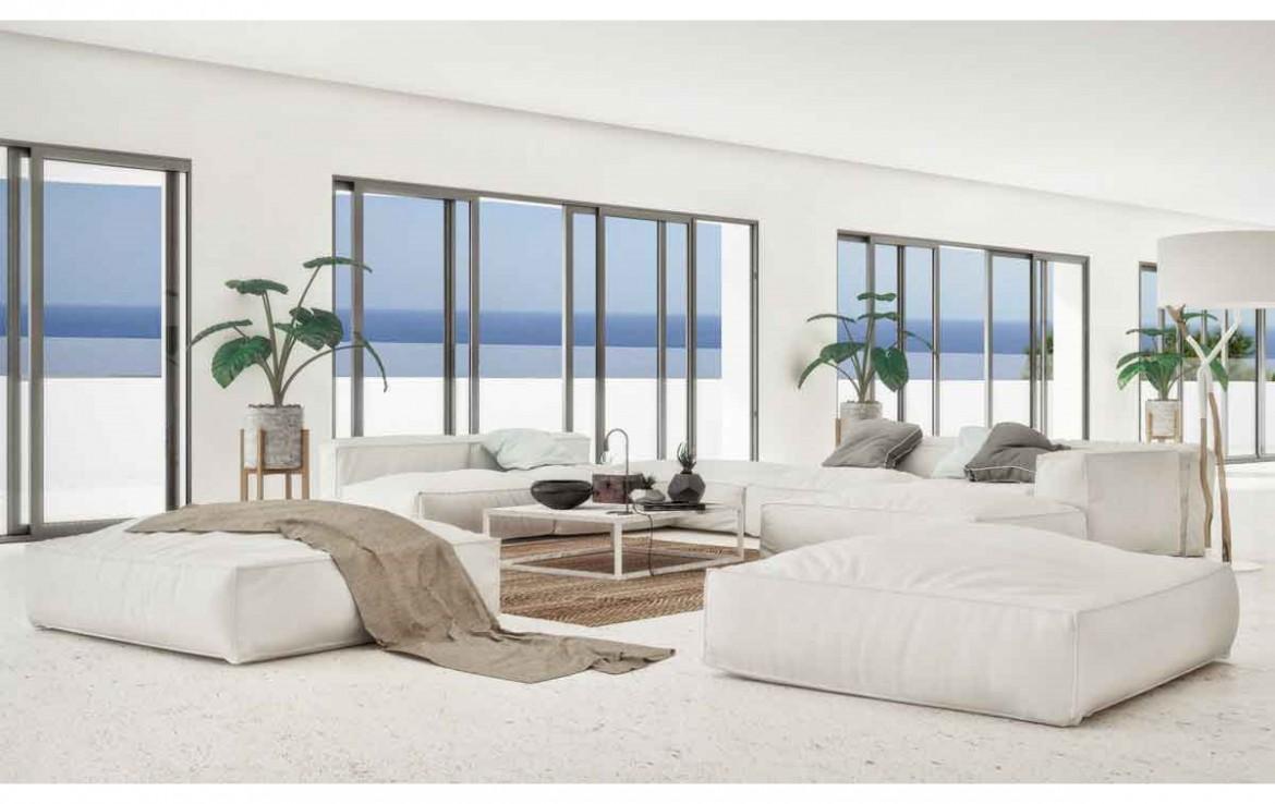 Minimalistische woonkamer met witte modulaire banken, lichte natuurstenen vloer en grote glazen schuifdeuren met uitzicht op de Middellandse Zee.