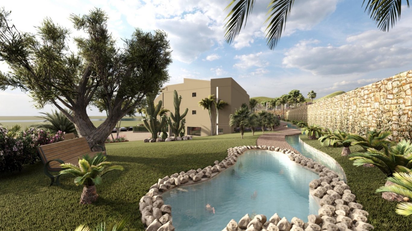Aangelegde tuinen met een vijver met stenen randen, slingerende paden en mediterrane beplanting zoals olijfbomen en cactussen bij het hotelgebouw.