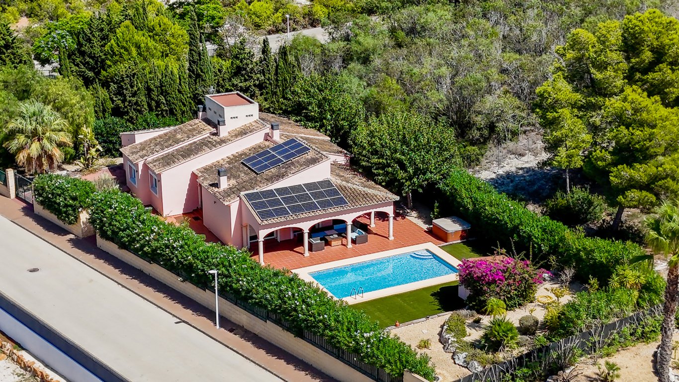 Luchtfoto van de villa met zonnepanelen, privézwembad en een overdekte naya met bogen, omgeven door een volgroeide mediterrane tuin.