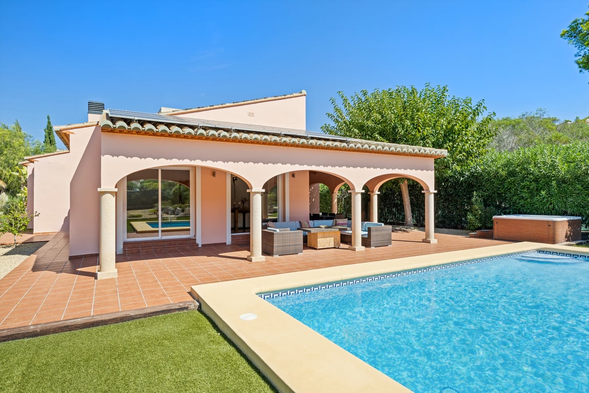 Exterieur van de villa met een overdekte naya met bogen, terracotta terras, mozaïekzwembad, zonnepanelen op het dak en een buitenjacuzzi.