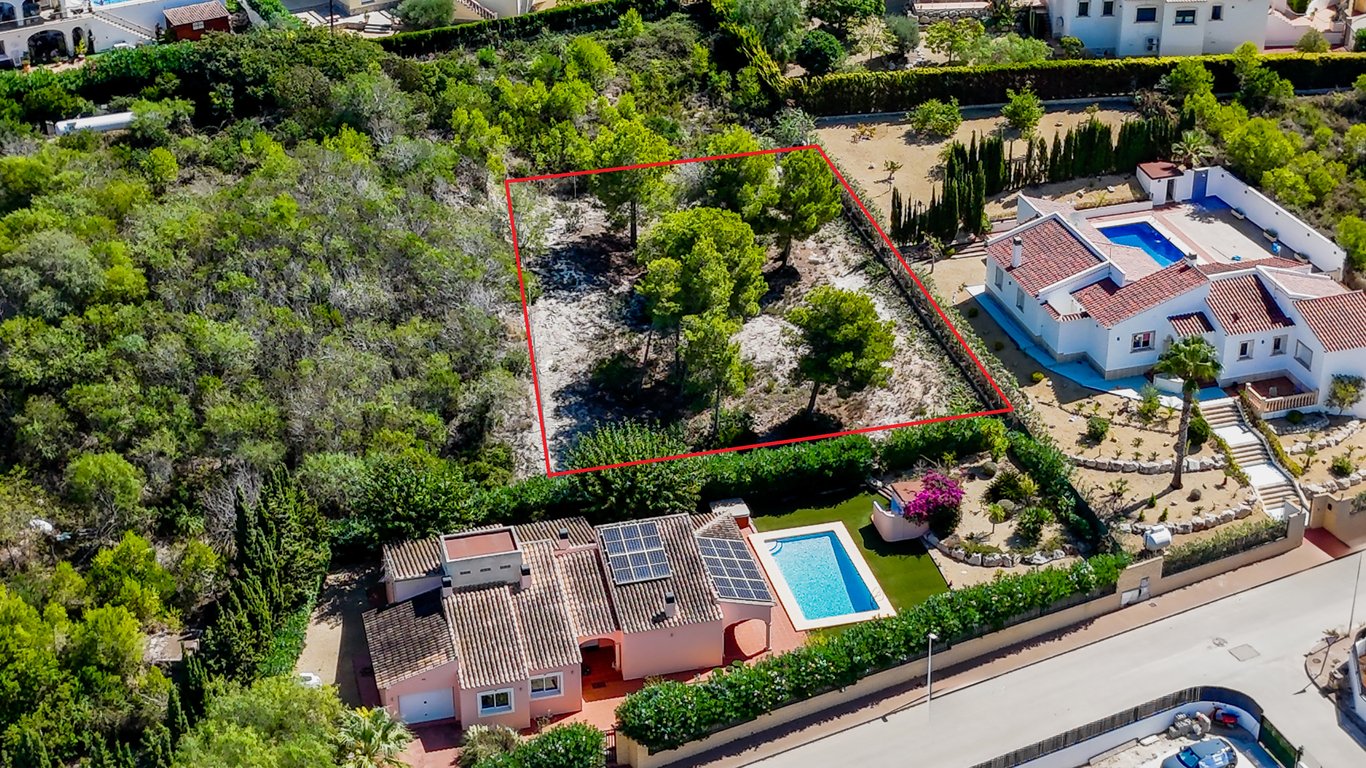 Luchtfoto van de villa met zonnepanelen en zwembad, inclusief het aangrenzende bouwperceel met volwassen pijnbomen, rood omkaderd.