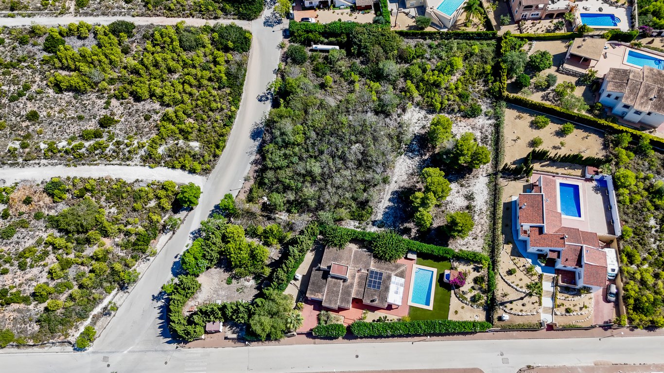Luchtfoto van de villa met zonnepanelen en zwembad, inclusief het grote naastgelegen bouwperceel met natuurlijke begroeiing in Jávea.