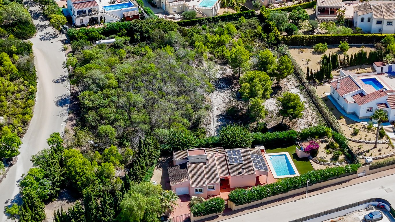 Luchtfoto van de villa met zonnepanelen, zwembad en het naastgelegen beboste bouwperceel in een rustige woonwijk in Jávea.