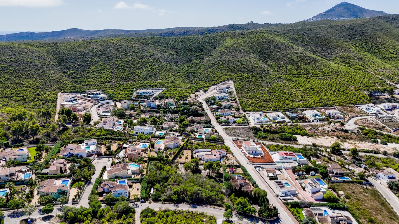 Luchtfoto van de woonwijk in Jávea, met een duidelijk overzicht van de villa's met zwembad tegen de achtergrond van de groene, beboste heuvels.