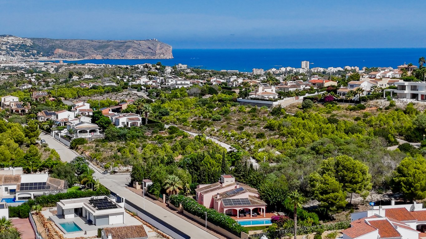 Panoramisch luchtfoto van de villa met zonnepanelen en zwembad, gelegen in een groene woonwijk met weids uitzicht over de Middellandse Zee en de kustlijn.
