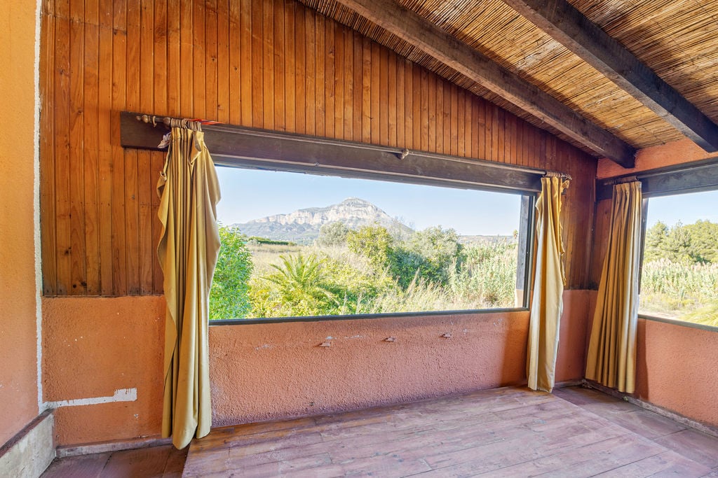 Binnenruimte met houten lambrisering en een rieten plafond, met een weids uitzicht op de Montgó-berg door een groot horizontaal raam.