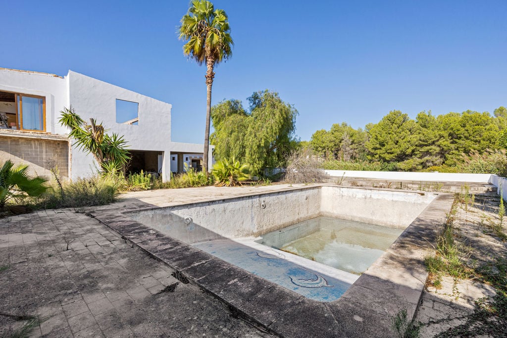 Groot buitenzwembad met mozaïekdetails en een uitgestrekt terras, omgeven door mediterrane bomen en een wit gebouw met een modern ontwerp.