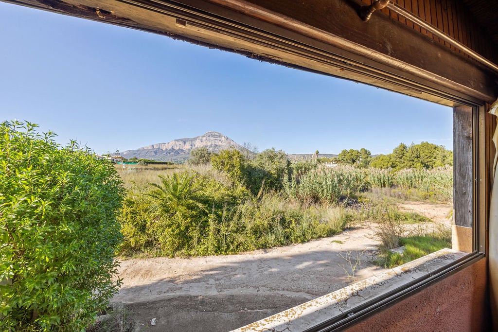Panoramisch uitzicht op de Montgó-berg door een raam met houten kozijn. De buitenruimte is voorzien van mediterrane beplanting en een heldere horizon.