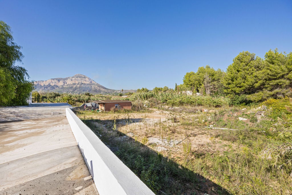 Panoramisch uitzicht op de Montgó-berg vanaf een verhoogd betonnen terras, uitkijkend over een vlak perceel met mediterrane beplanting.