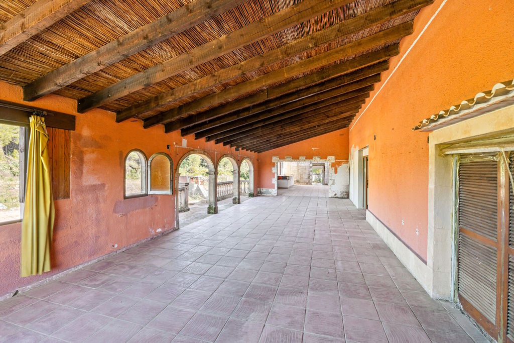 Ruim overdekt terras met traditionele houten balken, rieten plafond, terracotta muren en klassieke stenen bogen met uitzicht op het terrein.
