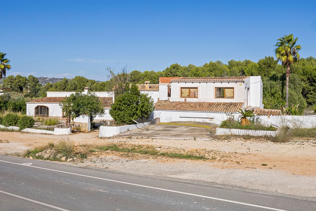 Vooraanzicht van het traditionele mediterrane gebouw met witgekalkte muren en pannendaken, gelegen op een groot perceel aan de hoofdweg.