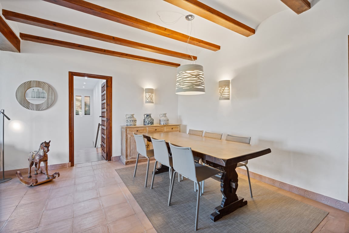 Eethoek met authentieke houten plafondbalken, ambachtelijke tegelvloer en een massief houten tafel, verlicht door eigentijdse designlampen.