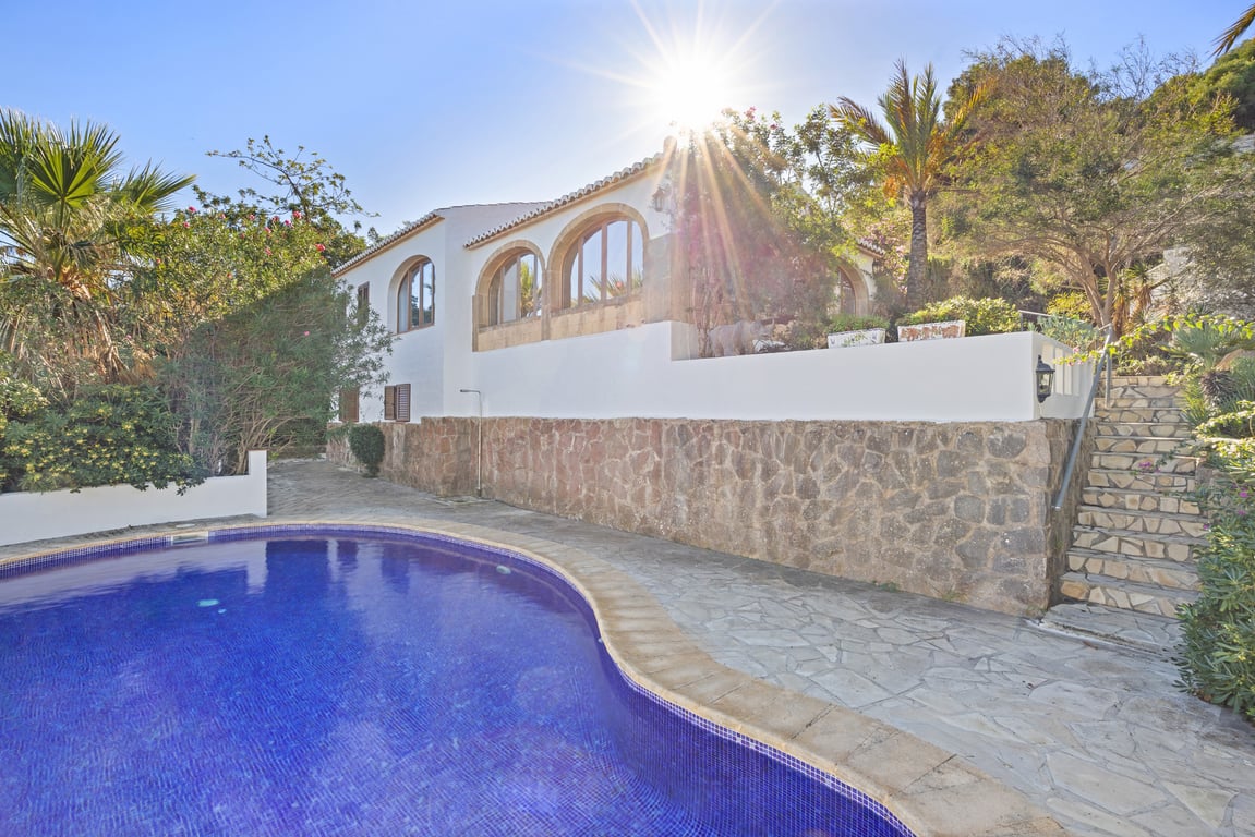 Exterieur van de villa met privézwembad, natuurstenen muren en een naya met bogen van Tosca-steen onder de mediterrane zon.