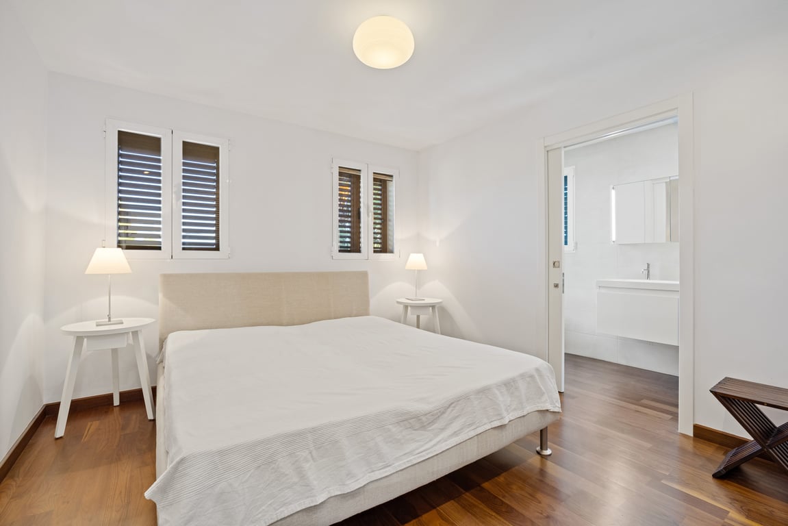Gerenoveerde slaapkamer met donkere houten vloer, stoffen hoofdbord en schuifdeur naar een moderne en-suite badkamer met zwevend wastafelmeubel.