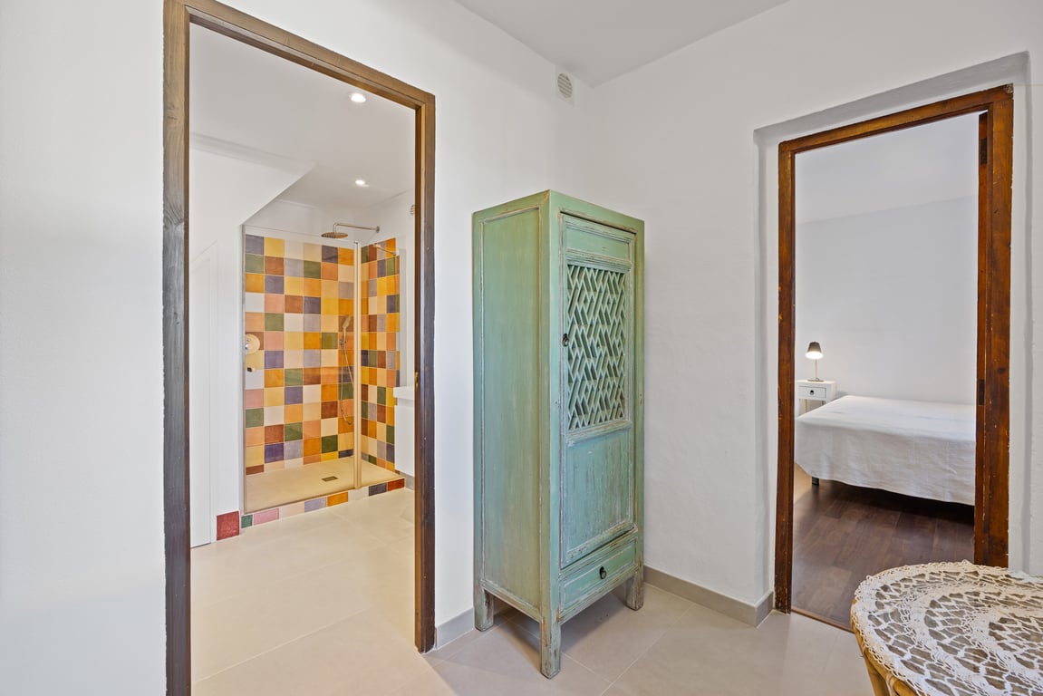 Hal met een rustieke groene kast, die een slaapkamer verbindt met een moderne badkamer met kleurrijke handgemaakte tegels.