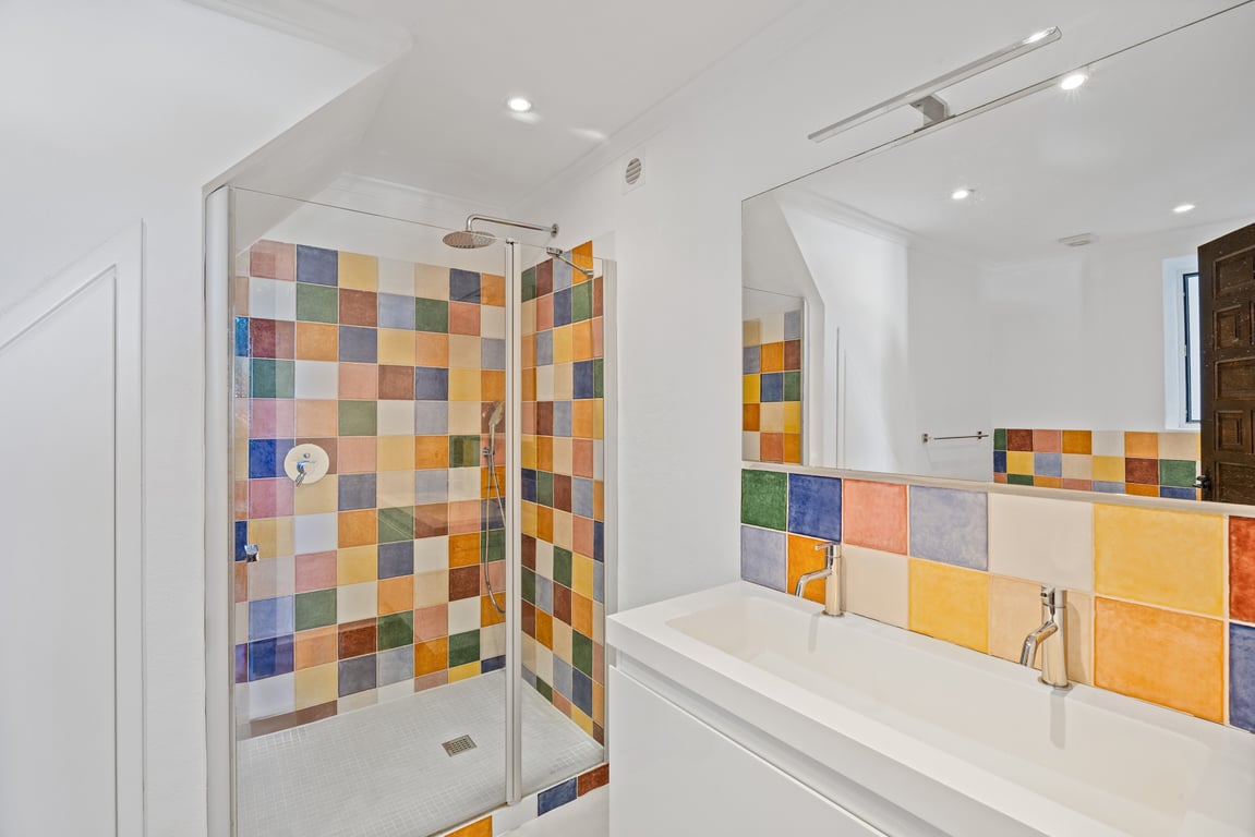 Moderne badkamer met dubbele wastafel en glazen douchewand, voorzien van kleurrijke keramische tegels en ingebouwde plafondverlichting.