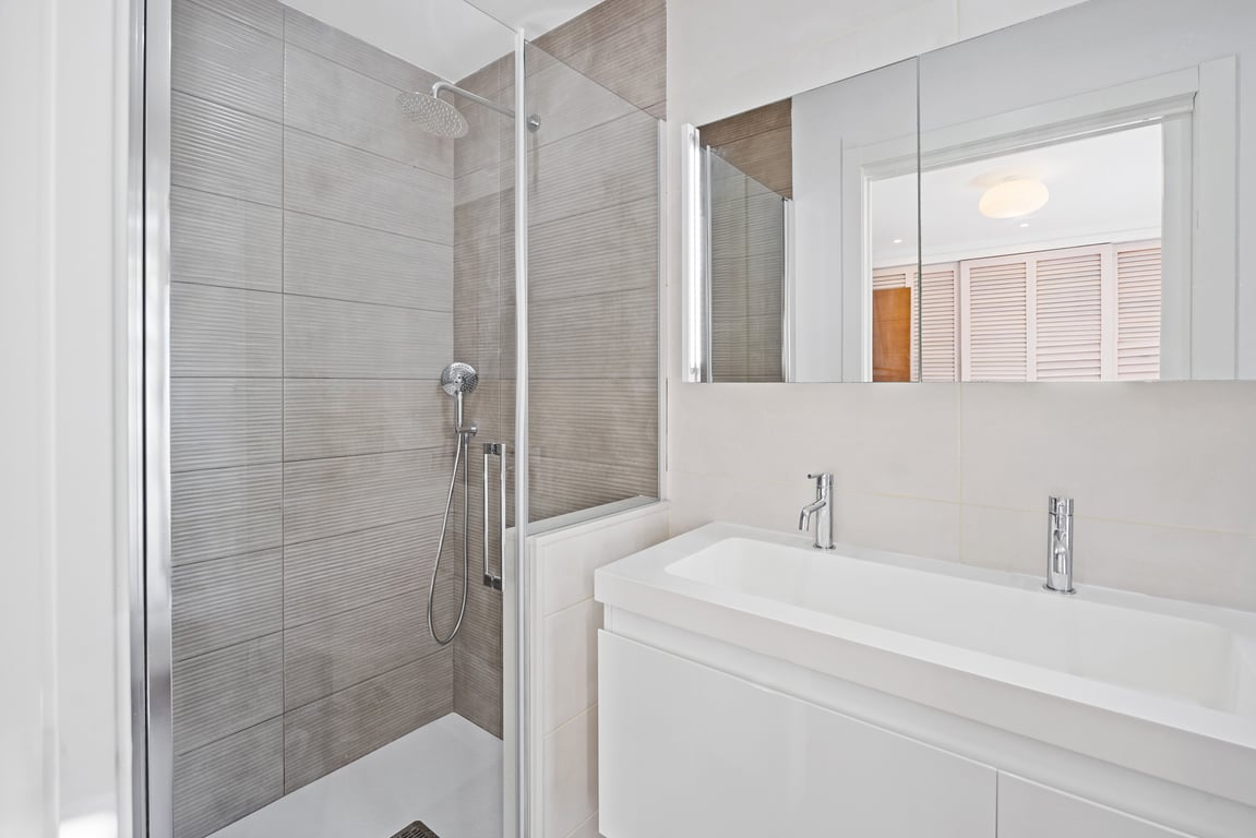 Moderne badkamer met inloopdouche, grijze structuurtegels, glazen wand en een strak wit wastafelmeubel met eigentijdse chromen kranen.