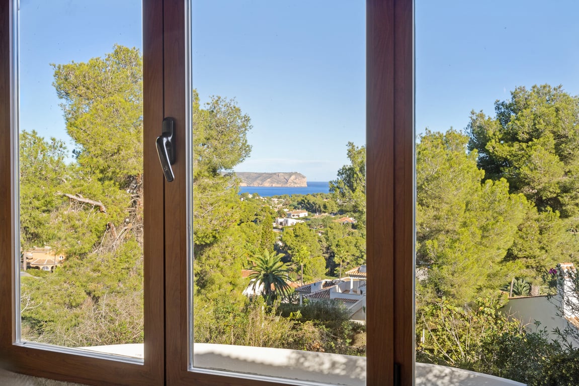 Panoramisch uitzicht op zee en de kaap door een houten kozijn met dubbele beglazing, uitkijkend over mediterrane pijnbomen.