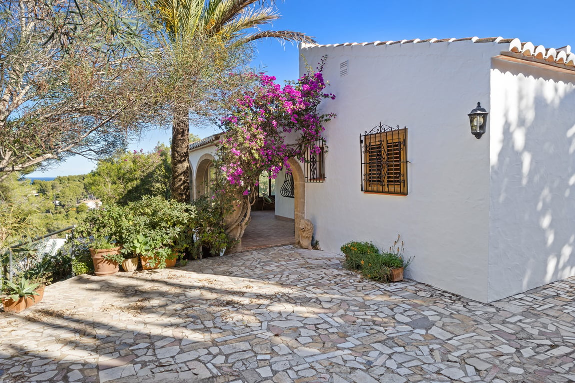 Traditionele witte gevel met Tosca stenen bogen, bloeiende bougainville en een terras van natuursteen met uitzicht op de mediterrane omgeving.