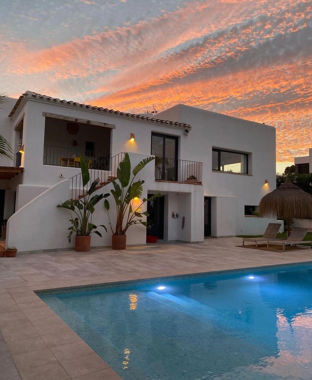 Exterieur in Ibiza-stijl bij schemering met verlicht zoutwaterzwembad, natuurstenen terras en mediterrane beplanting onder een kleurrijke zonsondergang.
