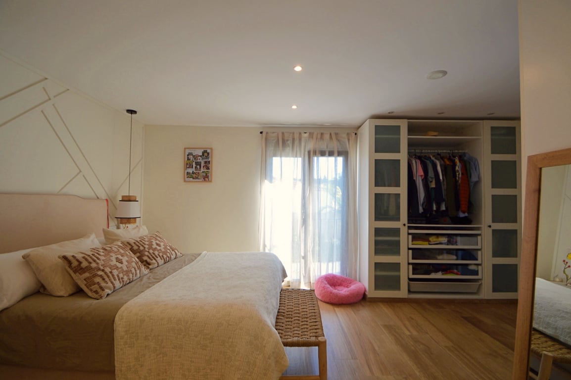 Lichte slaapkamer met houten vloer, een geometrische accentmuur en een inbouwkast met matglazen deuren en geïntegreerde opbergruimte.