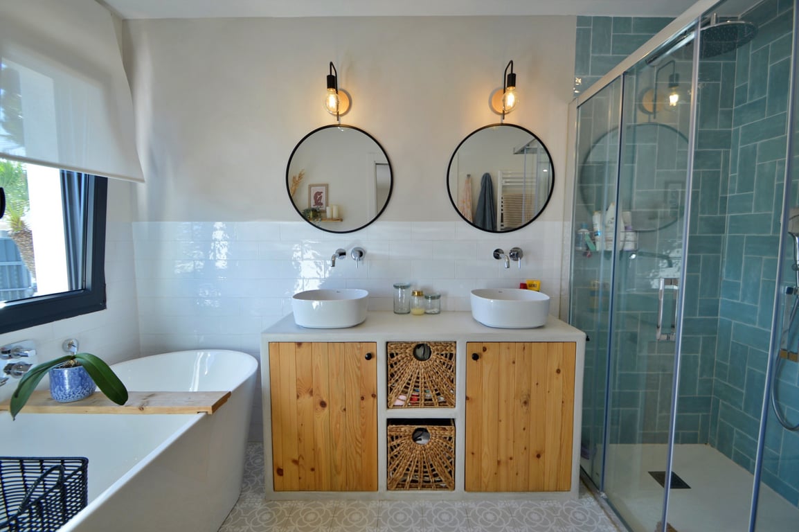 Moderne badkamer met dubbele wastafel, houten kasten, een vrijstaand bad en een inloopdouche met opvallende turquoise tegels en glazen wand.