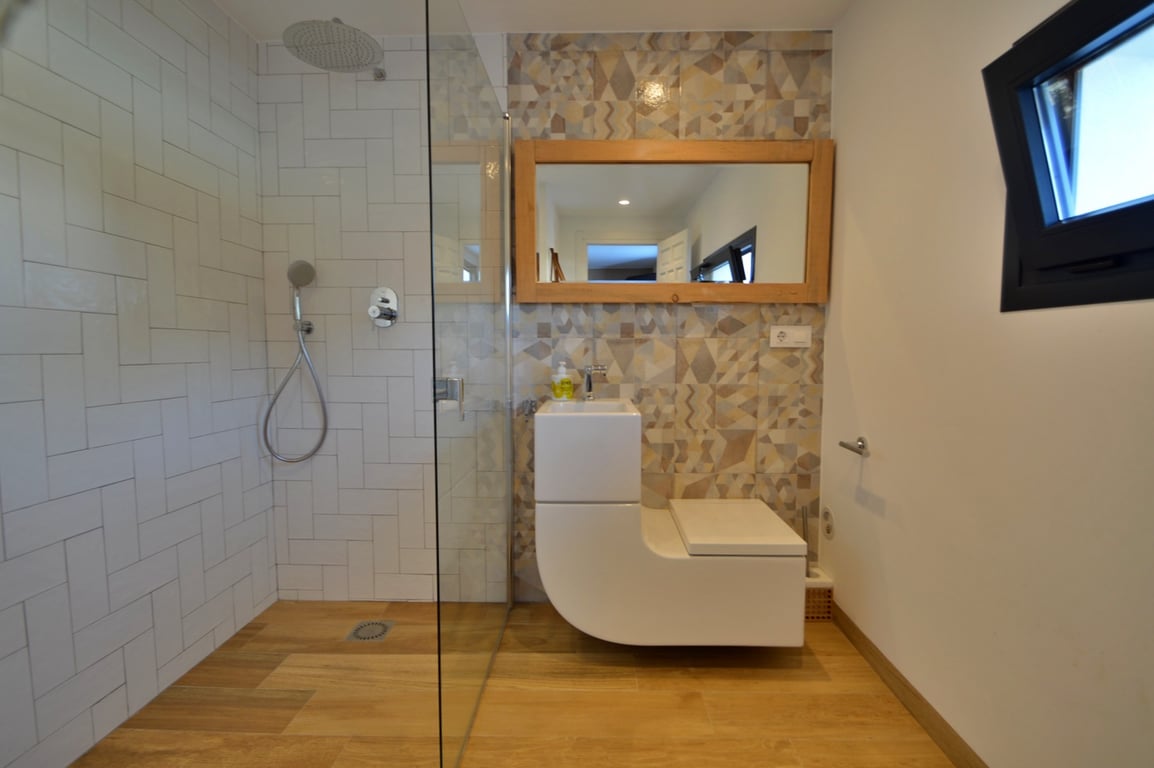 Moderne badkamer met inloopdouche, glazen wand en een uniek geïntegreerd wastafel-toiletmeubel. Voorzien van geometrische accenttegels en een spiegel met houten lijst.
