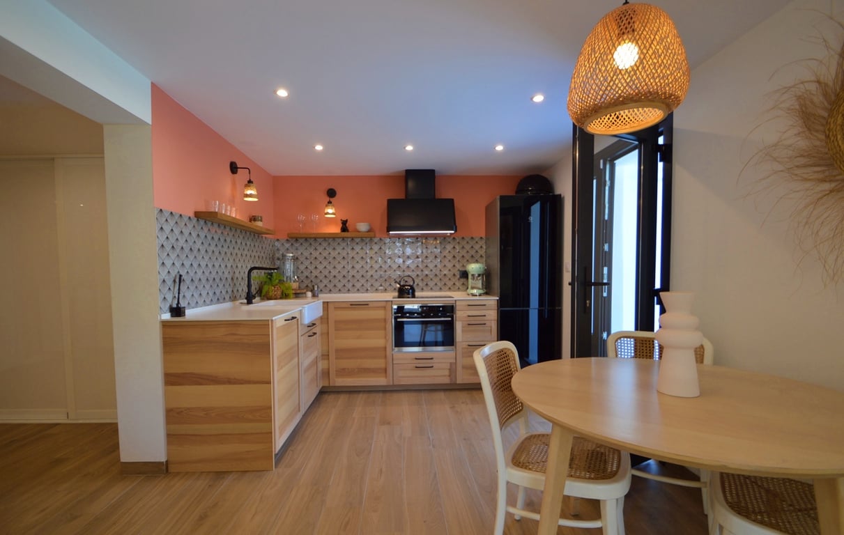 Moderne keuken met houten kasten, een terracotta accentmuur en een eethoek met ronde tafel, rotan stoelen en een hanglamp van natuurlijke vezels.