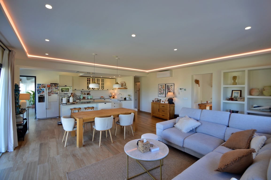Open woon- en eetkamer met een moderne keuken, indirecte LED-plafondverlichting, lichte houten vloeren en een stijlvolle, neutrale inrichting.