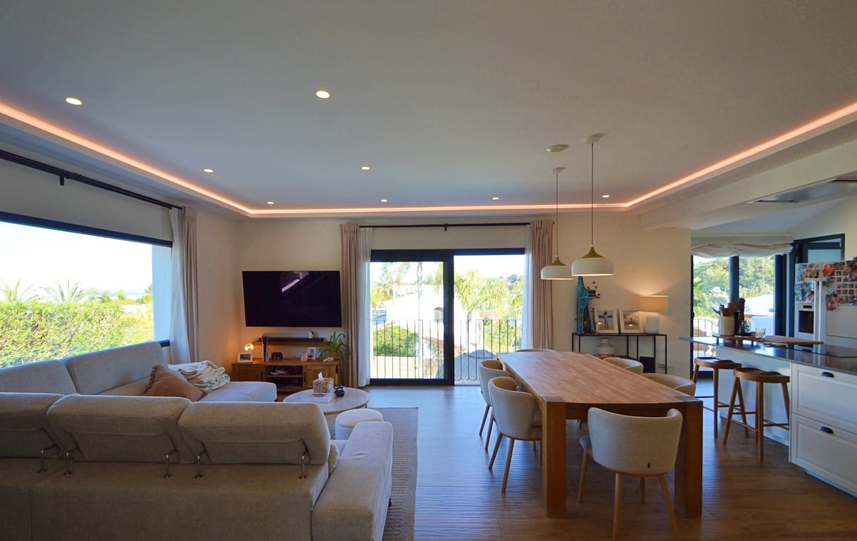 Open woon- en eetkamer met indirecte LED-verlichting, een robuuste houten eettafel en grote schuifpui die zorgt voor een naadloze verbinding met buiten.