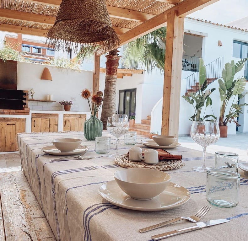 Overdekt buitenterras met houten pergola en rieten dak, voorzien van een buitenkeuken met ingebouwde barbecue in mediterrane stijl.