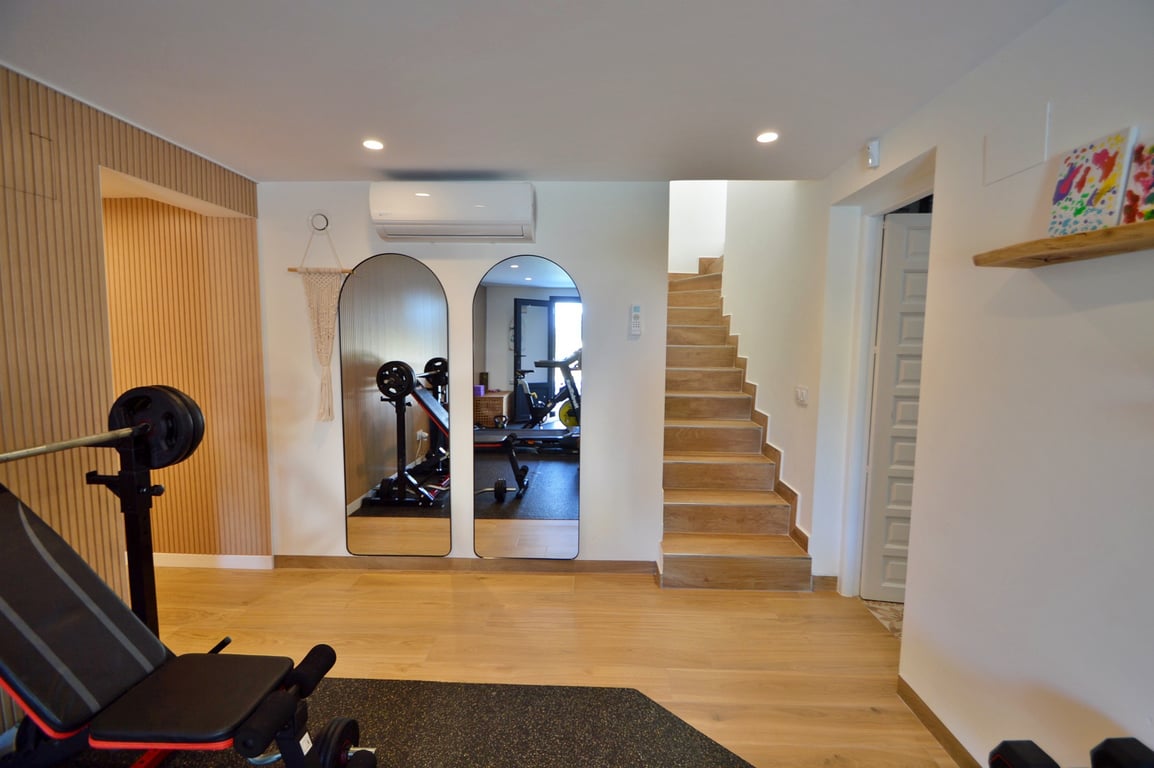 Privé fitnessruimte met boogspiegels, houtlook vloer, airconditioning en een vaste trap, ontworpen voor optimaal comfort en functionaliteit.