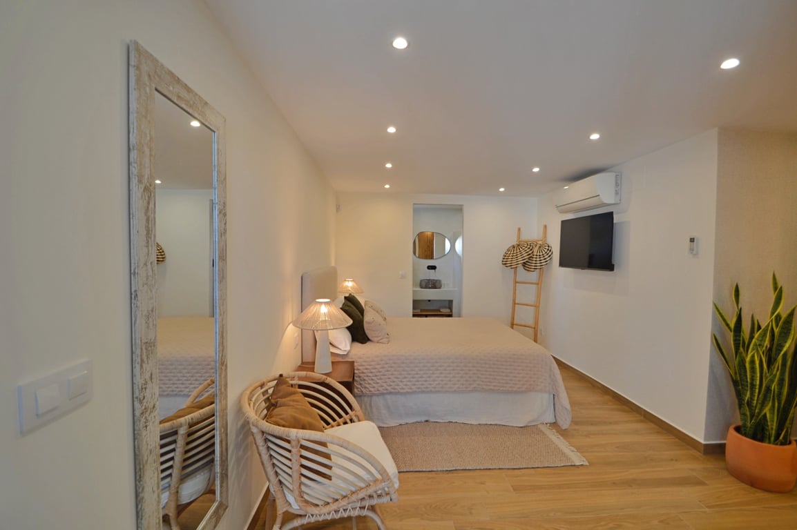 Slaapkamer in Ibiza-stijl met houtlook vloer, LED-inbouwspots, airconditioning en een modern geïntegreerde ensuite badkamer.