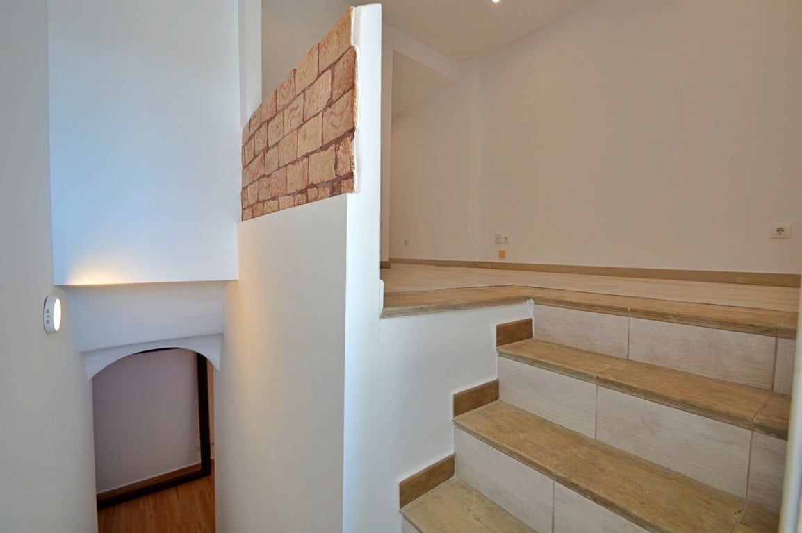 Binnentrap met keramische tegels in houtlook, witte muren en een decoratieve bakstenen wand die de verschillende woonlagen scheidt.