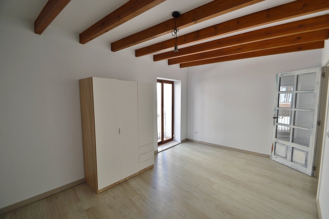 Gerenoveerde kamer met originele houten plafondbalken, lichte houten vloer en toegang tot het balkon. Inclusief een moderne kledingkast en een ambachtelijke houten glasdeur.
