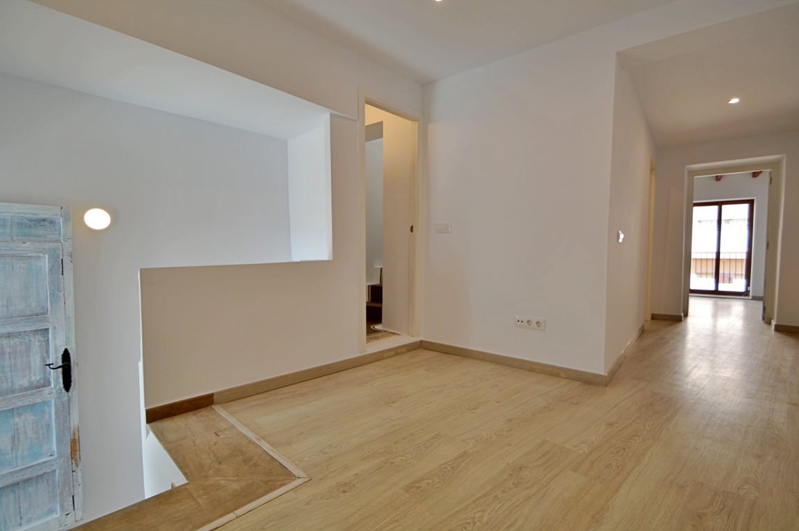 Lichte overloop met een lichte houten vloer, witte wanden en een gerestaureerde rustieke deur die karakter geeft aan de moderne ruimte.