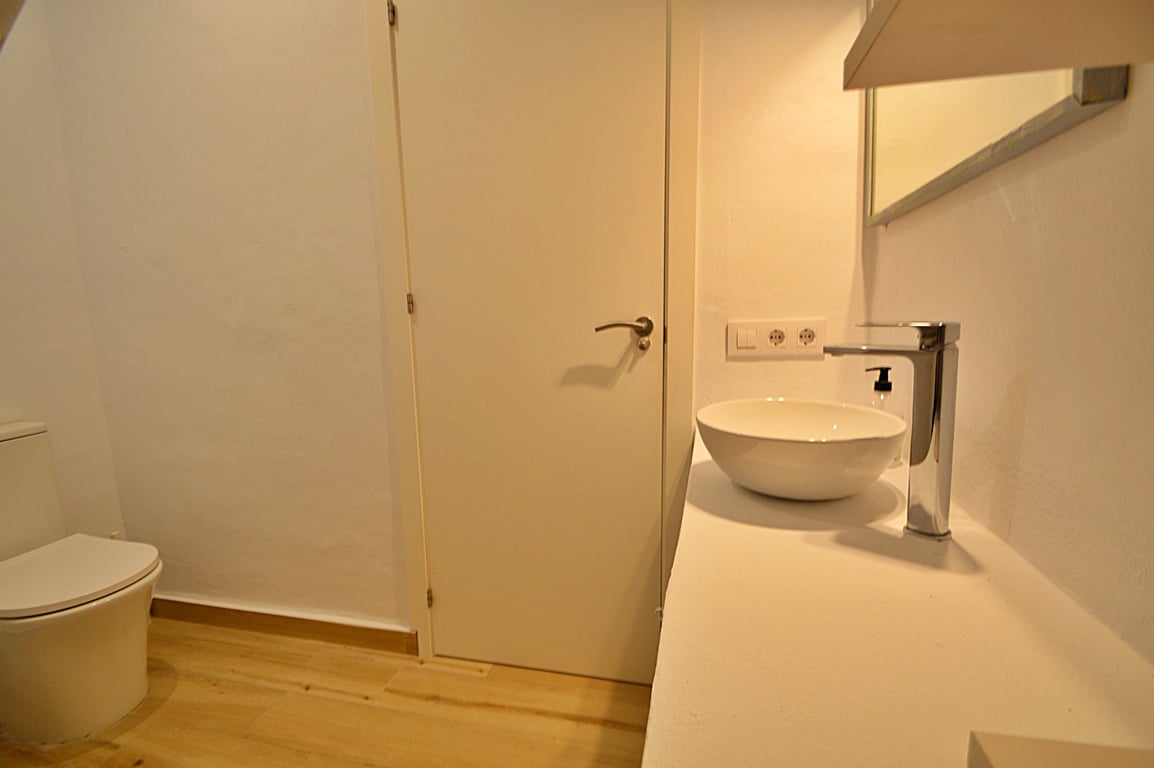 Moderne badkamer met een ronde opzetwastafel, chromen kraan en lichte houten vloer. Het minimalistische ontwerp heeft witte wanden en eigentijds sanitair.