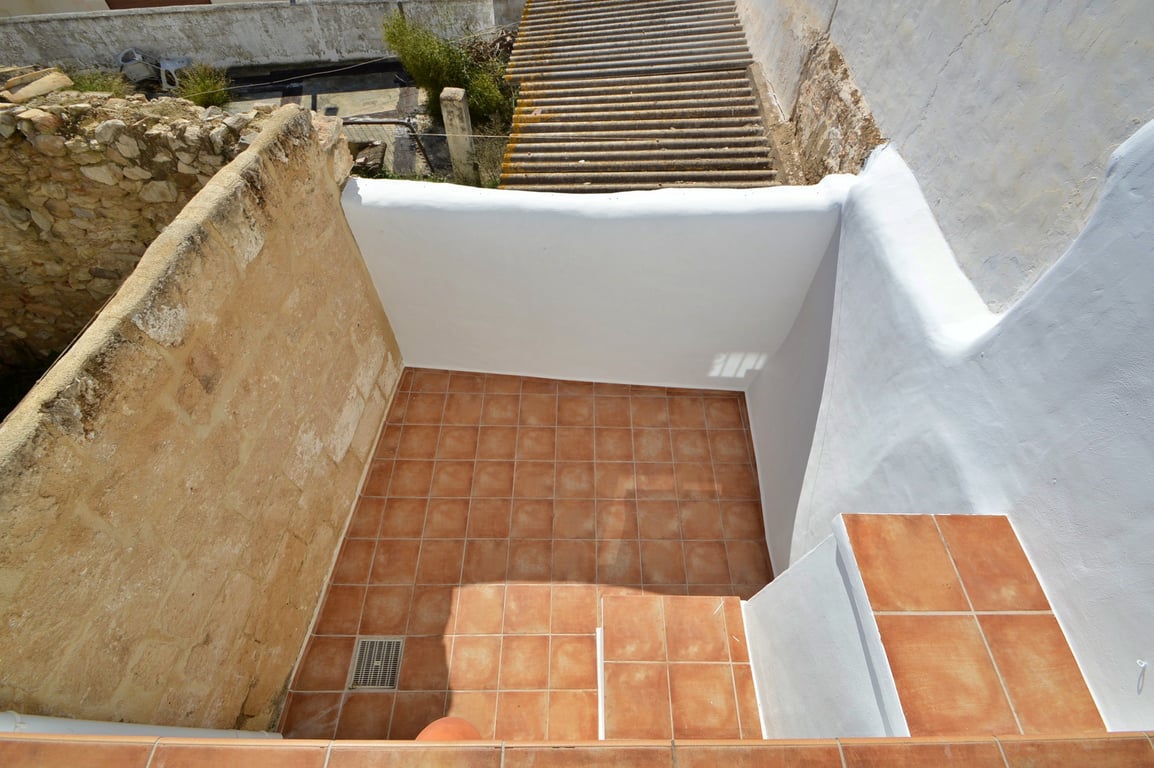 Privéterras voorzien van terracotta vloertegels, witgekalkte muren en een authentieke natuurstenen zijmuur die het rustieke karakter behoudt.