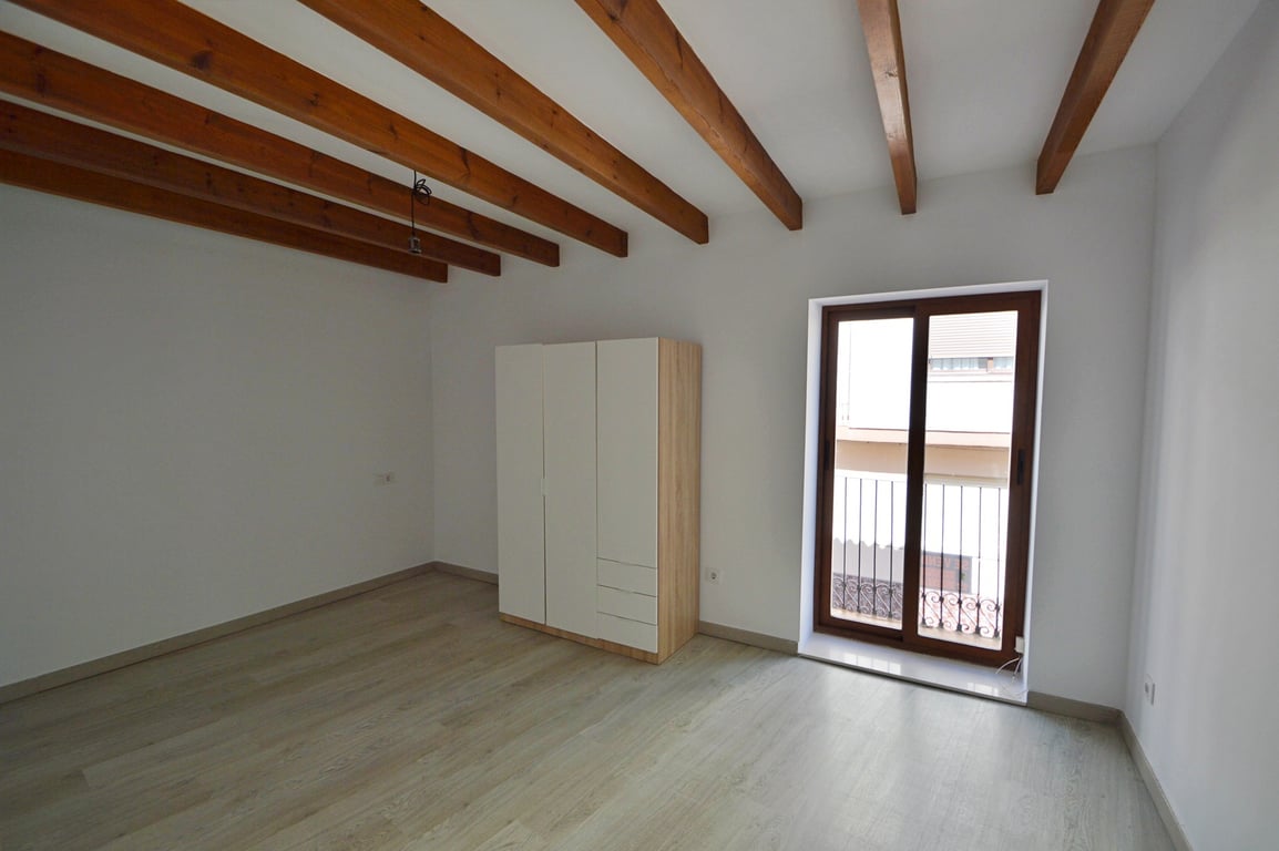 Slaapkamer met authentieke houten plafondbalken, lichte laminaatvloer en een moderne kast. Een glazen schuifdeur biedt toegang tot een privébalkon.